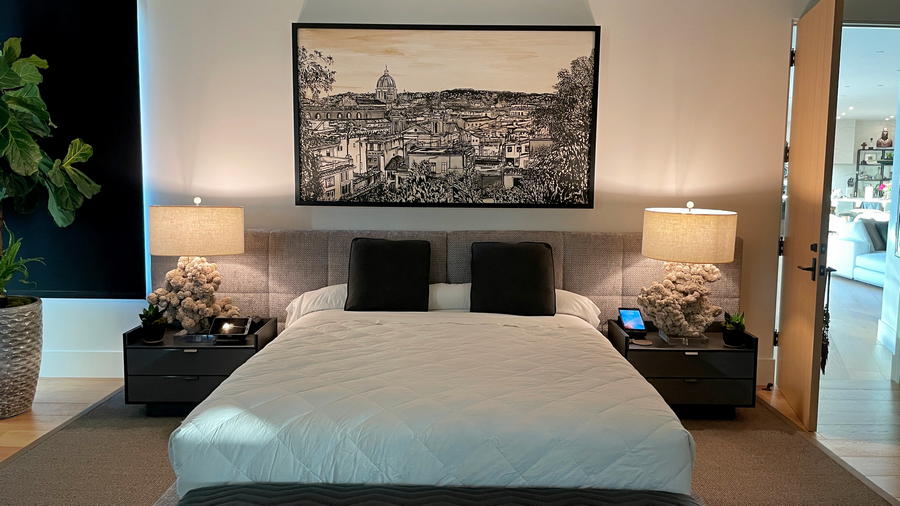 A sold large black and white painting of Rome painted by artist Brooke Harker hanging on a wall over a bed in a modern home