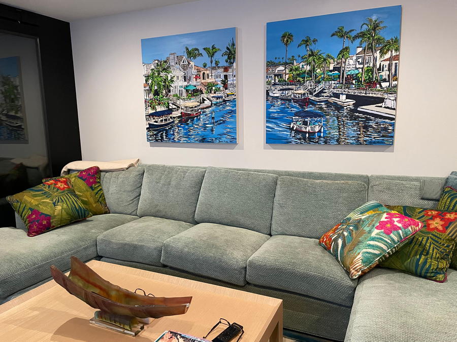 Two original oil paintings of Newport Beach harbor, homes by the water with boats painted by artist Brooke Harker hanging on a wall over a sofa in a California coastal home.