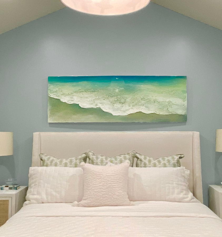 Long horizontal contemporary coastal seascape beach painting by artist Dasha Guilliam hanging on the wall over a bed in a coastal decor style home.