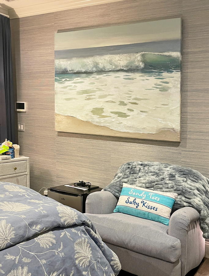Contemporary coastal beach and wave painting by artist Dasha Guilliam hanging on bedroom wall in beach house.